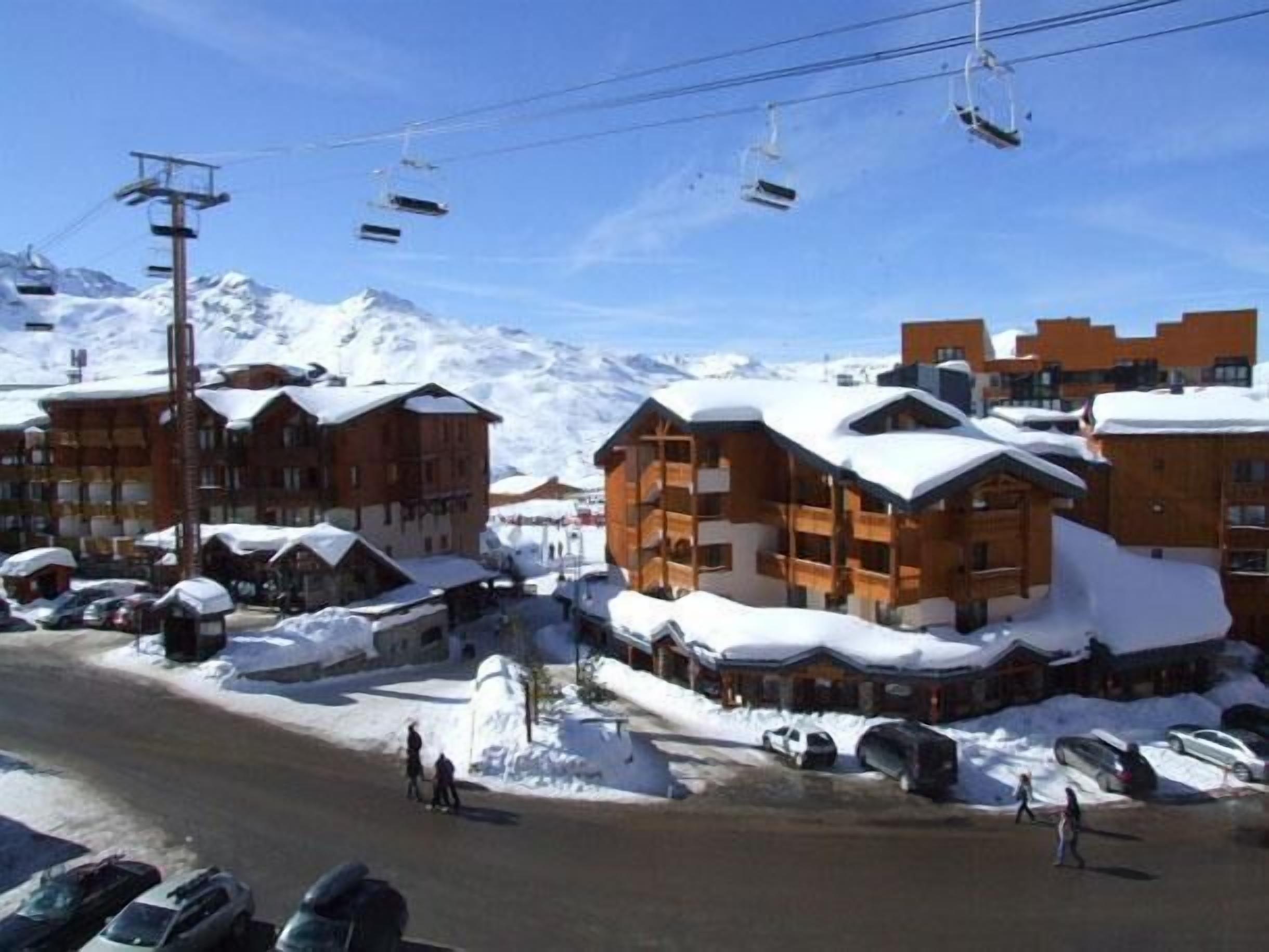 En snötäckt semesteranläggning med trähus, en skidlift och parkerade bilar.