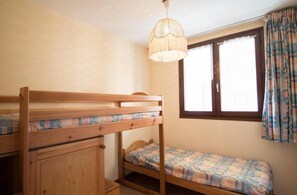 Une pièce avec des lits superposés, une armoire en bois, un luminaire suspendu et une fenêtre avec des rideaux.