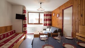 A cozy room with a bed, a sofa, a dining table set with plates and glasses, a television, and a window with curtains. - 300m from ski slopes, 1st floor, balcony, tv, ski locker, 41m², Val Cenis (Lanslebourg-Mont-Cenis)