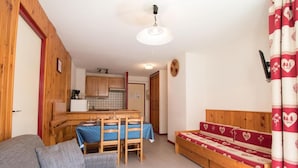 A cozy room with a wooden sofa, a dining table with chairs, a kitchenette, and a bed with heart-patterned bedding. - 300m from ski slopes, 1st floor, balcony, tv, ski locker, 41m², Val Cenis (Lanslebourg-Mont-Cenis)