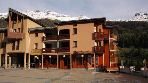A multi-story building with a ground floor shop and upper floors with balconies, set against a mountainous backdrop. - Floor -1, terrace, tv, ski locker, 25m², Val Cenis (Lanslevillard)