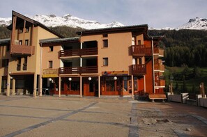 A multi-story building with a ground floor shop and upper floors with balconies, set against a mountainous backdrop. - 100m from ski slopes, floor -1, terrace, tv, ski locker, 25m², Val Cenis (Lanslevillard)