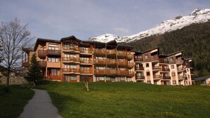 A multi-story hotel with balconies, a paved pathway, and a mountainous backdrop. - Floor -1, terrace, tv, ski locker, 25m², Val Cenis (Lanslevillard)