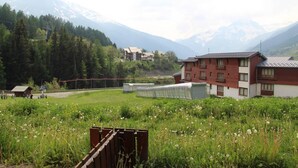 A building with a red and white facade, surrounded by a green field and mountains in the background. - Floor -1, terrace, tv, ski locker, 25m², Val Cenis (Lanslevillard)