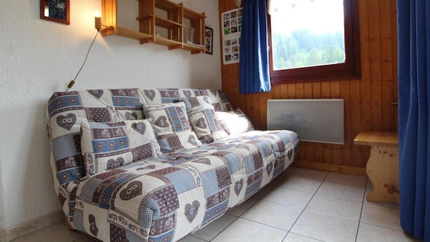 Una habitación acogedora con un sofá de madera, una estantería montada en la pared y una ventana con vistas a árboles.