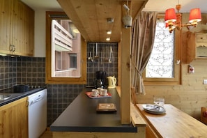 A kitchen with wooden cabinets, a black countertop, and a window with patterned curtains. - Ski-in/ski-out & foot of the slopes, 2nd floor, view ski slopes, balcony, tv, 35m², La Plagne (La Plagne)