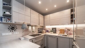 Une cuisine moderne avec des meubles en bois clair, un four encastré, un évier en acier inoxydable et un luminaire suspendu.