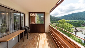 Un balcon avec un banc en bois, une table et une vue sur un paysage verdoyant avec des collines.