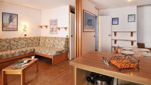 Een gezellige woonkamer met een bank, een houten salontafel en een eethoek met een tafel gedekt voor twee personen.