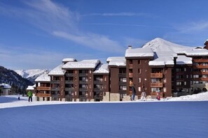 A ski resort with multi-story buildings, snow-covered roofs, and a clear blue sky. - Ski-in/ski-out & foot of the slopes, 4th floor, view ski slopes, balcony, tv, ski locker, 46m² (La Plagne)