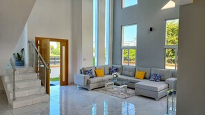 A spacious living room with a grey sofa set, a glass coffee table, and a staircase leading to an outdoor area.