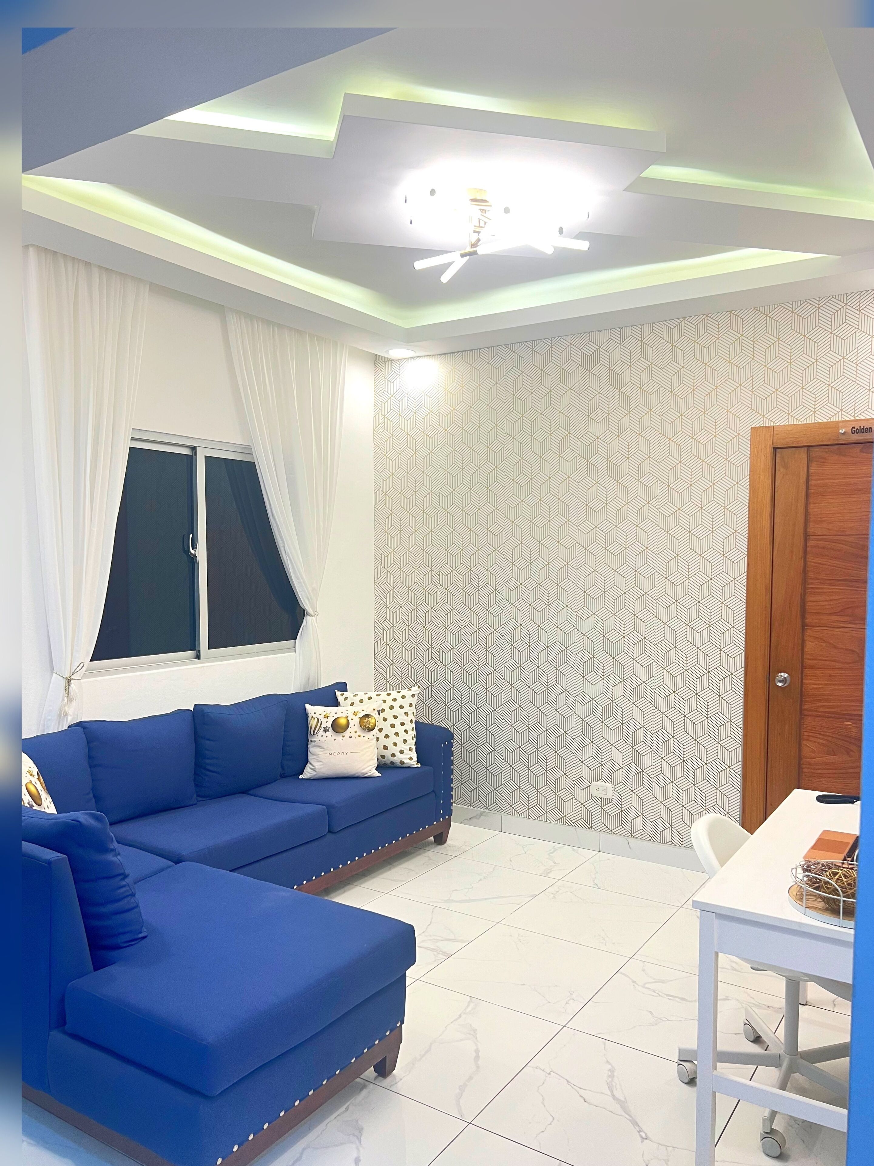 A modern living room with a blue sofa, a dining table, and a patterned wall.