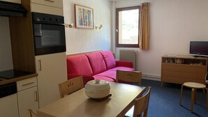 A compact living space with a kitchenette, a dining table, a red sofa, and a television. - 150m from ski slopes, 2nd floor, view resort, fitness, swimming pool, sauna, tv, ski locker, 26m² (Eaux-Bonnes)