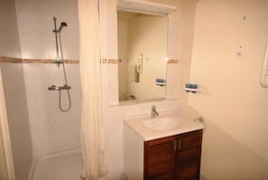 A bathroom with a shower, sink, mirror, and wooden cabinets.