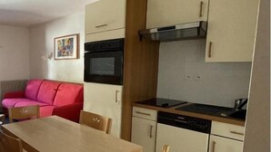 A compact kitchen with a dining table, a red sofa, and a painting on the wall. - 150m from ski slopes, 2nd floor, view resort, fitness, swimming pool, sauna, tv, ski locker, 29m² (Eaux-Bonnes)