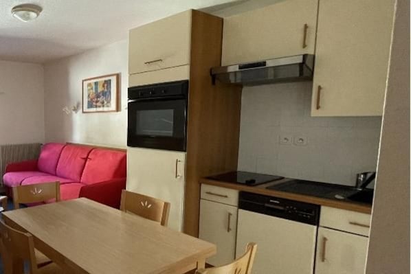 A compact kitchen with a dining table, a red sofa, and a painting on the wall.