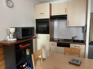 Cocina compacta con microondas, horno, lavamanos y una pequeña mesa de comedor.