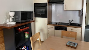 Kompakti keittiö, jossa on mikroaaltouuni, uuni, pesuallas ja pieni ruokapöytä.