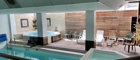 Een binnenzwembad met een jacuzzi en ligbedden.