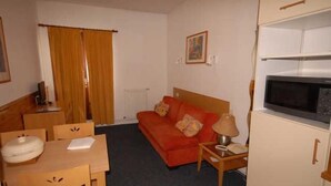 A compact hotel room with a single bed, a small table with a chair, a sofa, a microwave, and a radiator. - 150m from ski slopes, 1st floor, view resort, fitness, swimming pool, sauna, balcony, tv, ski locker (Eaux-Bonnes)