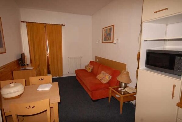 Une chambre d’hôtel de taille réduite, comprenant un lit simple, une petite table avec une chaise, un canapé, un four à micro-ondes et un radiateur.