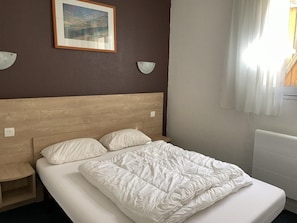A neatly made bed with a white comforter and pillows, a wooden headboard, and a small bedside table.