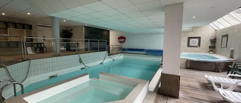 A swimming pool with a hot tub, lounge chairs, and a tiled floor.