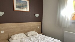 Un letto rifatto con un copriletto bianco e cuscini, una testiera in legno e un comodino.