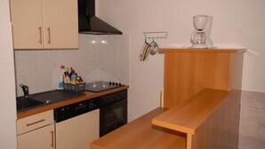 Una cucina con piano cottura, forno e lavello. Si nota un tavolo di legno e uno scaffale con una macchina da caffè.