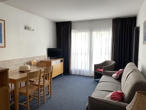 A compact hotel room with a dining area, a sofa, and a TV.
