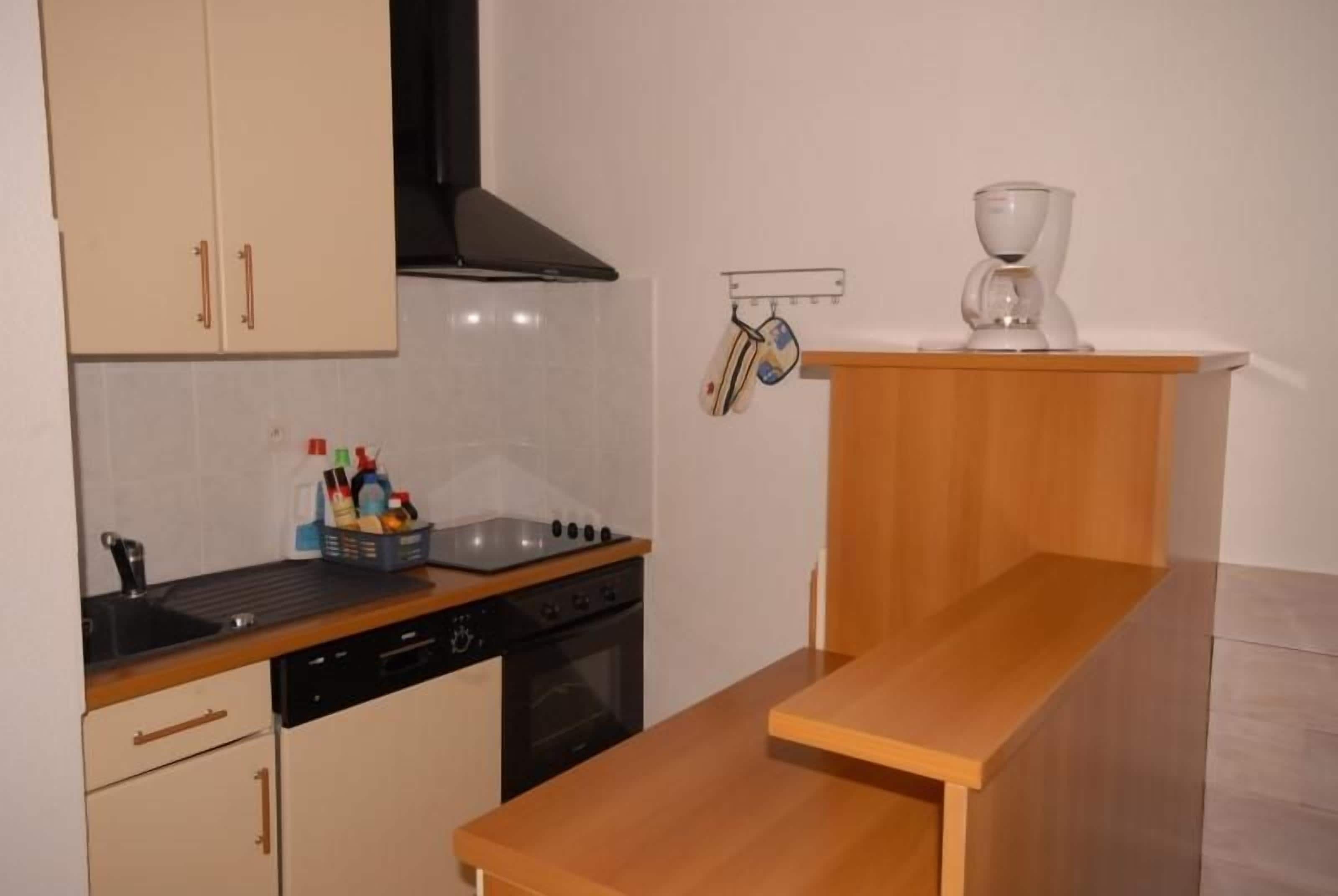 A kitchen with a stove, oven, and sink. There is a wooden table and a shelf with a coffee maker.