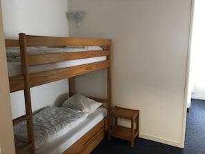 Ein Etagenbett mit Holzrahmen und weißer Bettwäsche, ein kleiner Nachttisch aus Holz sowie eine an der Wand befestigte Lampe.