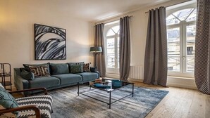A modern living room with a sofa, armchair, coffee table, and artwork on the wall. - Marais Rue de Turenne  and its very particular charming atmosphere.
 (Paris)