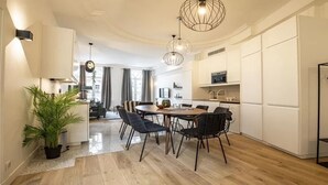 A modern kitchen with white cabinets, a dining area with a round table and chairs, and a hanging light fixture. - Marais Rue de Turenne  and its very particular charming atmosphere.
 (Paris)