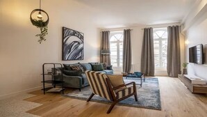 A modern living room with a sofa, a patterned armchair, a coffee table, and a hanging light fixture. - Marais Rue de Turenne  and its very particular charming atmosphere.
 (Paris)