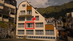 A multi-story hotel with balconies, a prominent red arrow pointing to a window, and a mountainous backdrop. - 150m from ski slopes, 2nd floor, view ski slopes, fitness, swimming pool, sauna, tv, ski locker (Eaux-Bonnes)