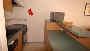 Cocina compacta con estufa a gas, horno y microondas. Un guante de cocina rojo cuelga en la pared, y una cesta tejida está sobre la encimera.