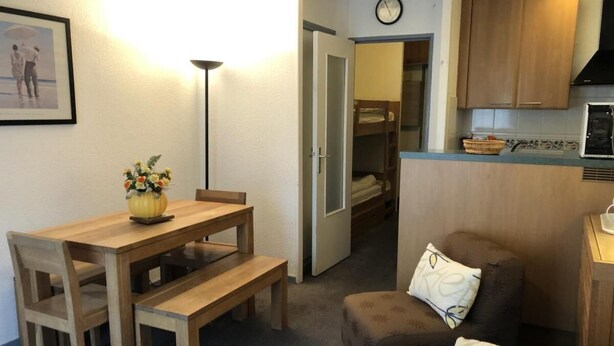 Un espacio habitable compacto con una mesa de comedor, un sofá, una pequeña cocina y una puerta que da a un dormitorio.