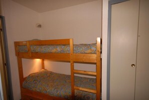 Una cama litera con ropa de cama estampada en una habitación con una puerta y un accesorio de iluminación en la pared.