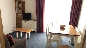 Une pièce comprenant une table à manger, des chaises, un canapé, un téléviseur et une bibliothèque.