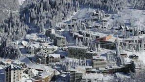 Une station de ski enneigée, composée de plusieurs bâtiments, dont des hôtels et peut-être un centre de conférences, et entourée d’une forêt dense.