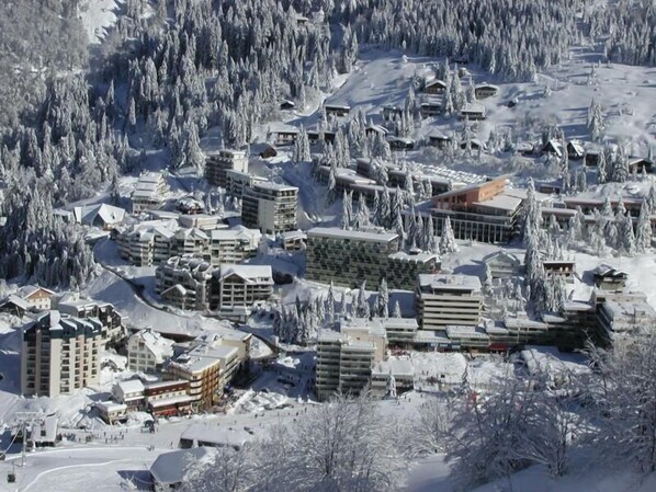 En snötäckt anläggning med flera byggnader, inklusive hotell och eventuellt ett konferenscenter, omgiven av tät skog.