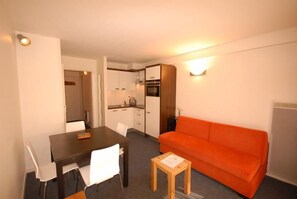 Un espace de vie compact comprenant une table à manger, des chaises, un canapé et un coin cuisine.