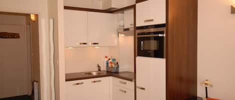 A compact kitchen with white cabinets, a built-in oven, and a sink.