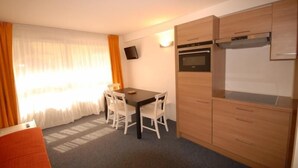 Eine kompakte Küche mit Esstisch und Stühlen, einem eingebauten Backofen und einem an der Wand montierten Fernseher.