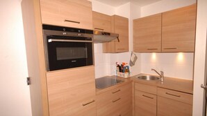 Eine kleine Küche mit Holdekor-Schränken, einem Backofen, einer Spüle und einer Arbeitsplatte mit einem Korb voller Reinigungsmittel.