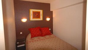 Ein kleines, ordentlich eingerichtetes Schlafzimmer mit einem Bett, zwei Kissen, einer Wandleuchte und einem gerahmten Bild.