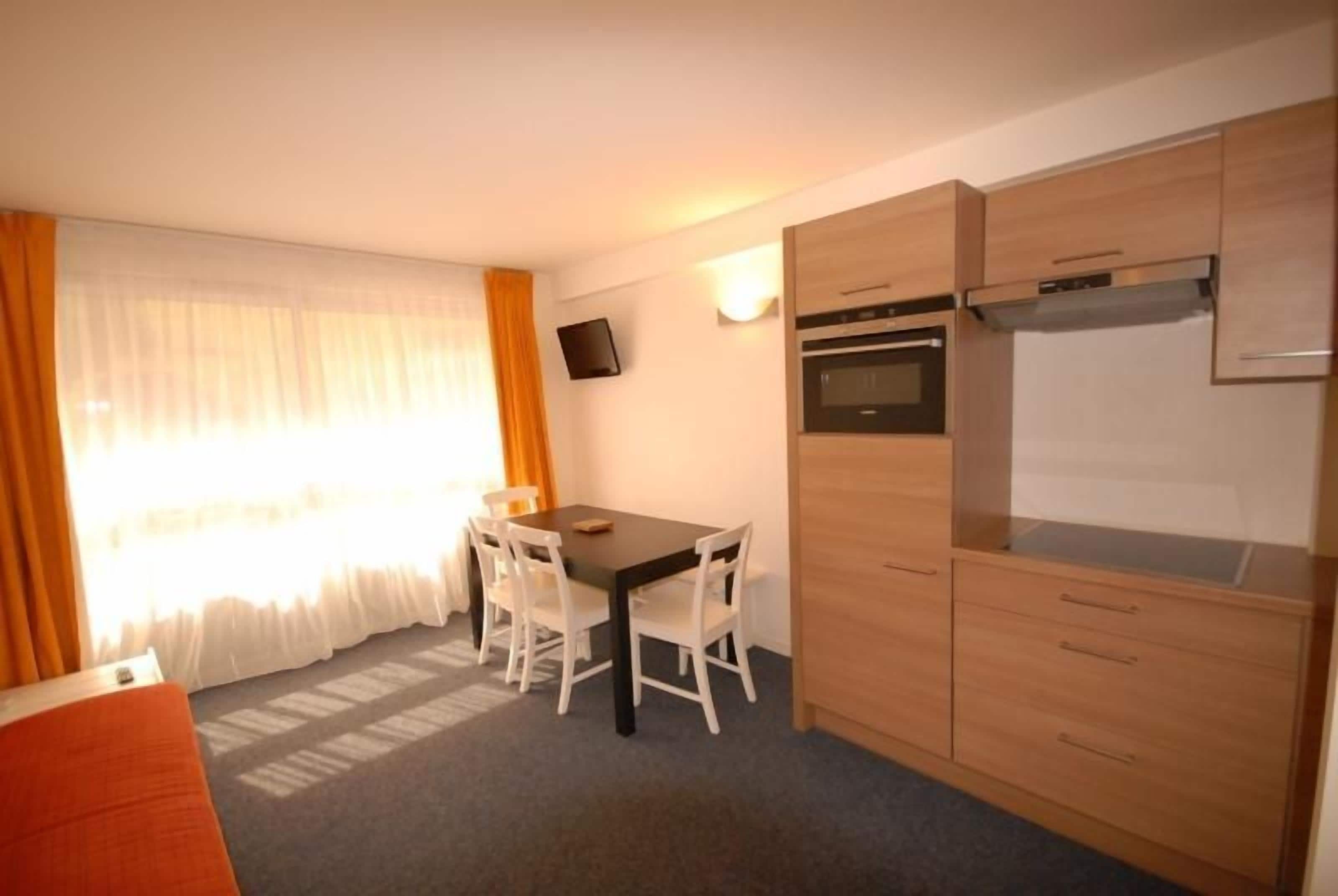 Une cuisine compacte comprenant une table et des chaises, un four encastré et un téléviseur fixé au mur.
