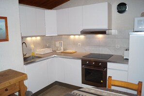 A compact kitchen with white cabinets, a built-in oven, a coffee maker, and a clock on the wall. - 20m from ski slopes, 4th floor, balcony, tv, 70m², Les 2 Alpes (Les Deux Alpes)