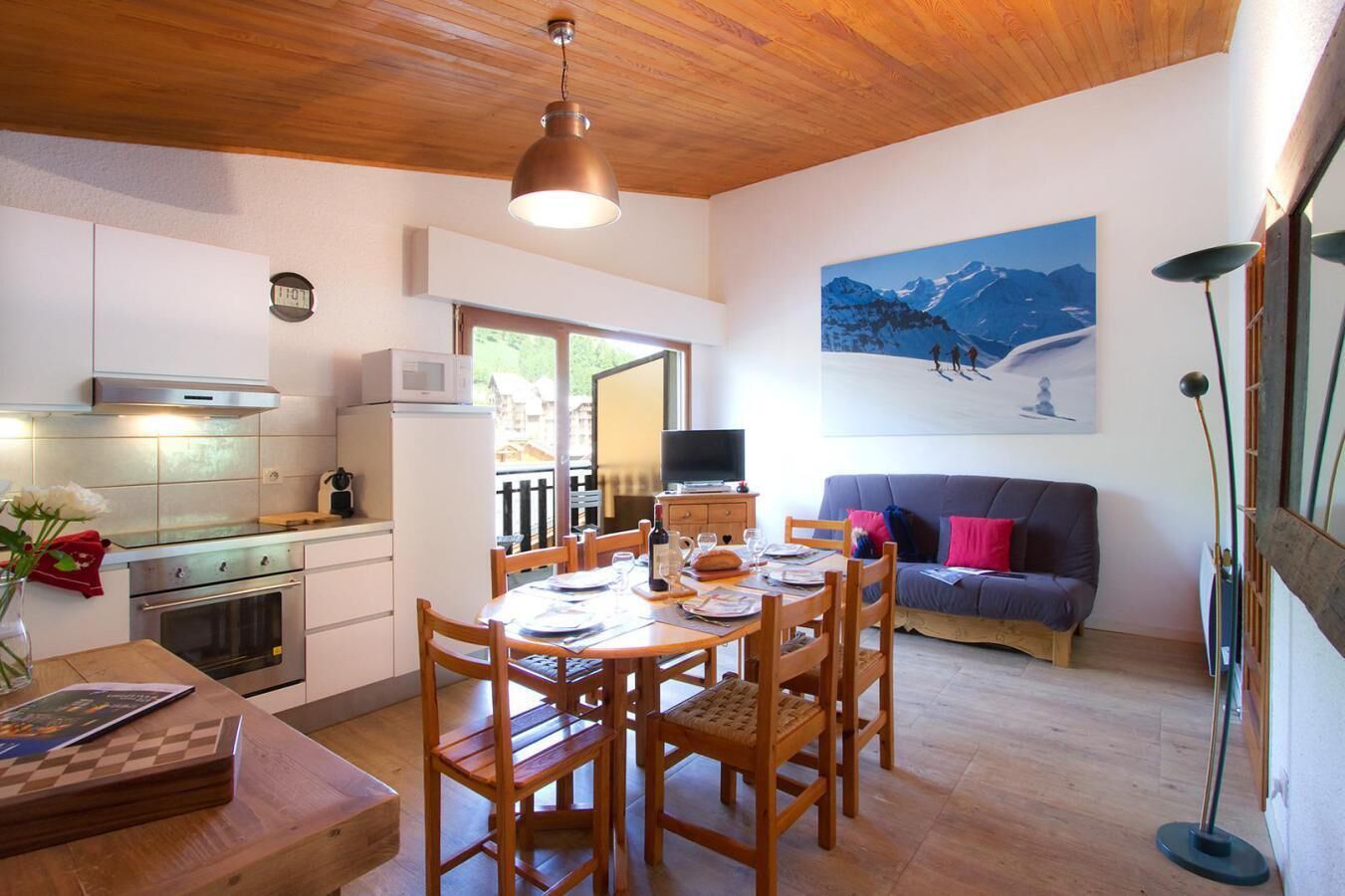 A compact kitchen with a dining area, a sofa, and a painting of mountains.